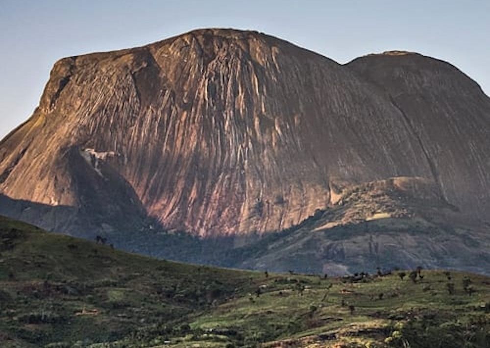 A large rocky mountain surrounded by grass and trees