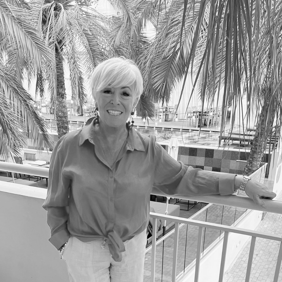 A woman is standing on a balcony with palm trees in the background.