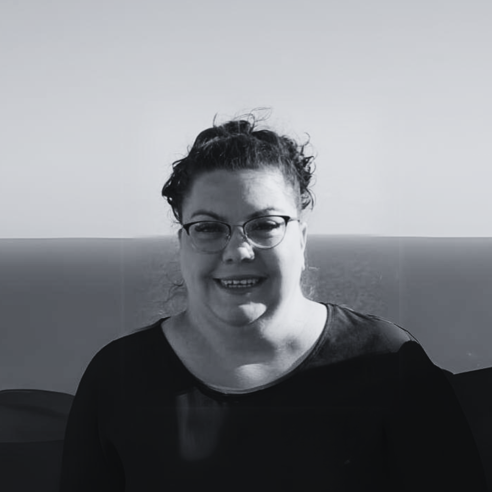 A woman wearing glasses is smiling in a black and white photo.