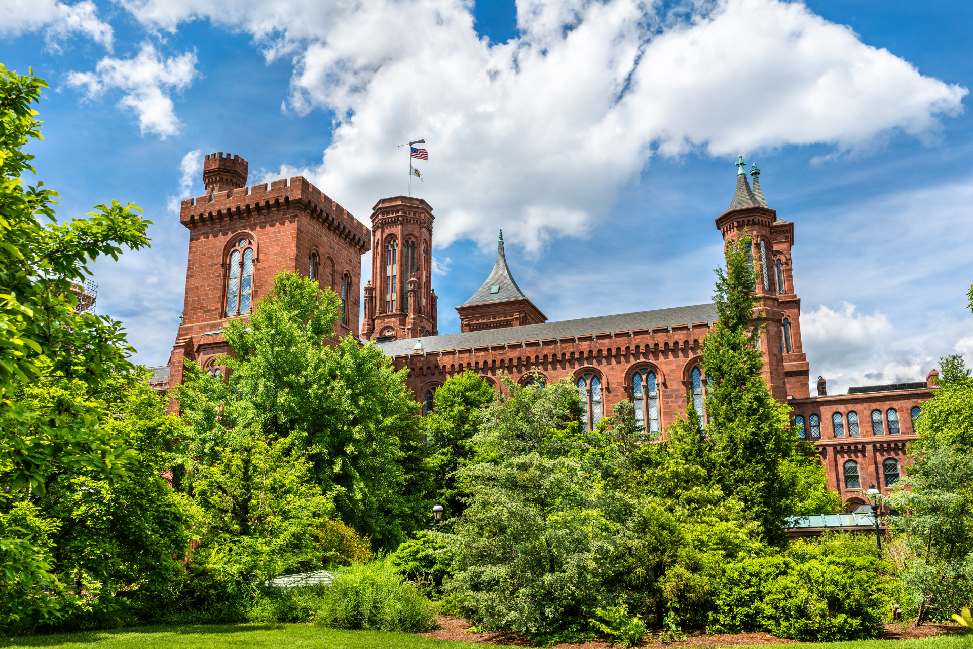 A large red brick building is surrounded by trees on a sunny day.