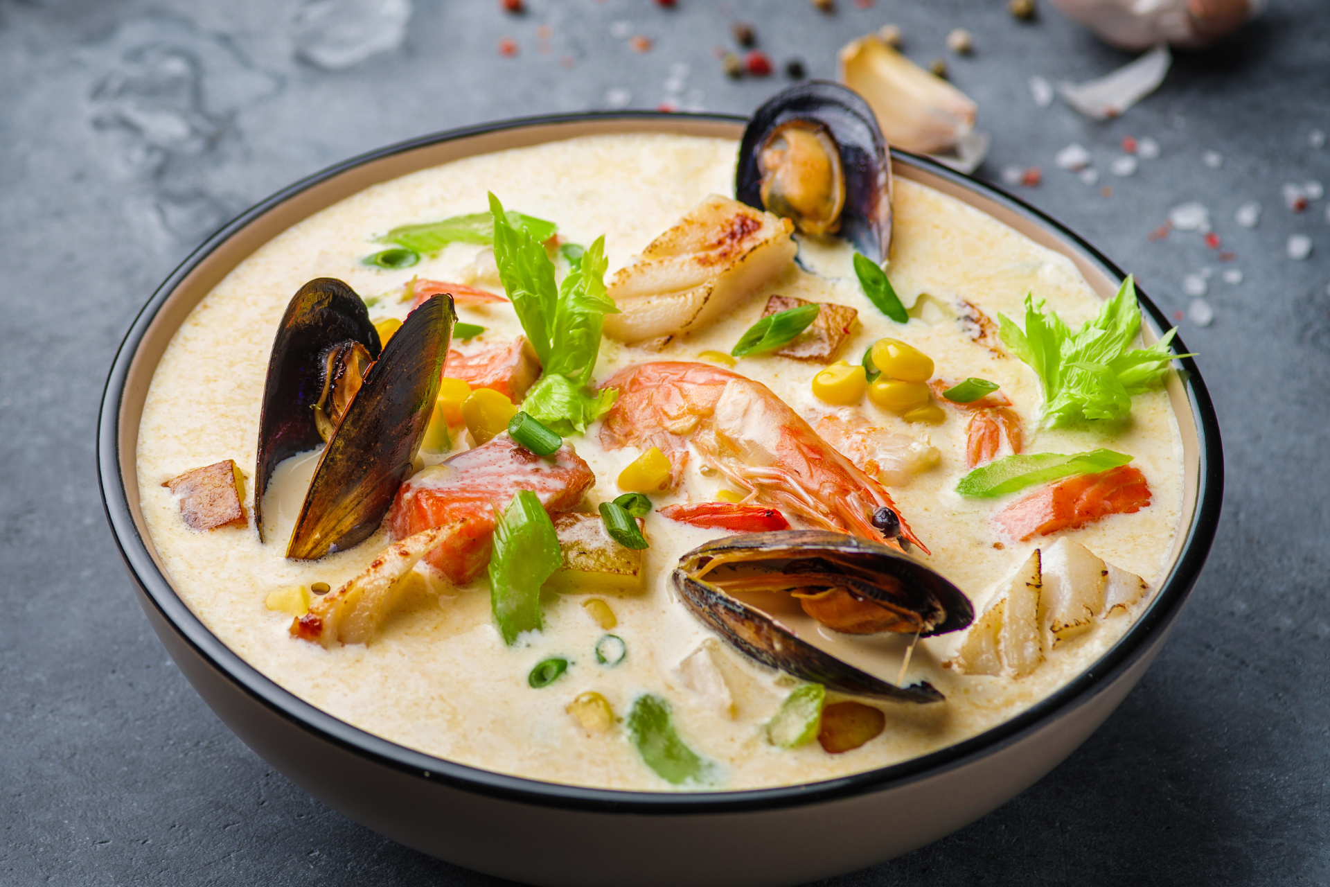 A bowl of soup with seafood and vegetables on a table.