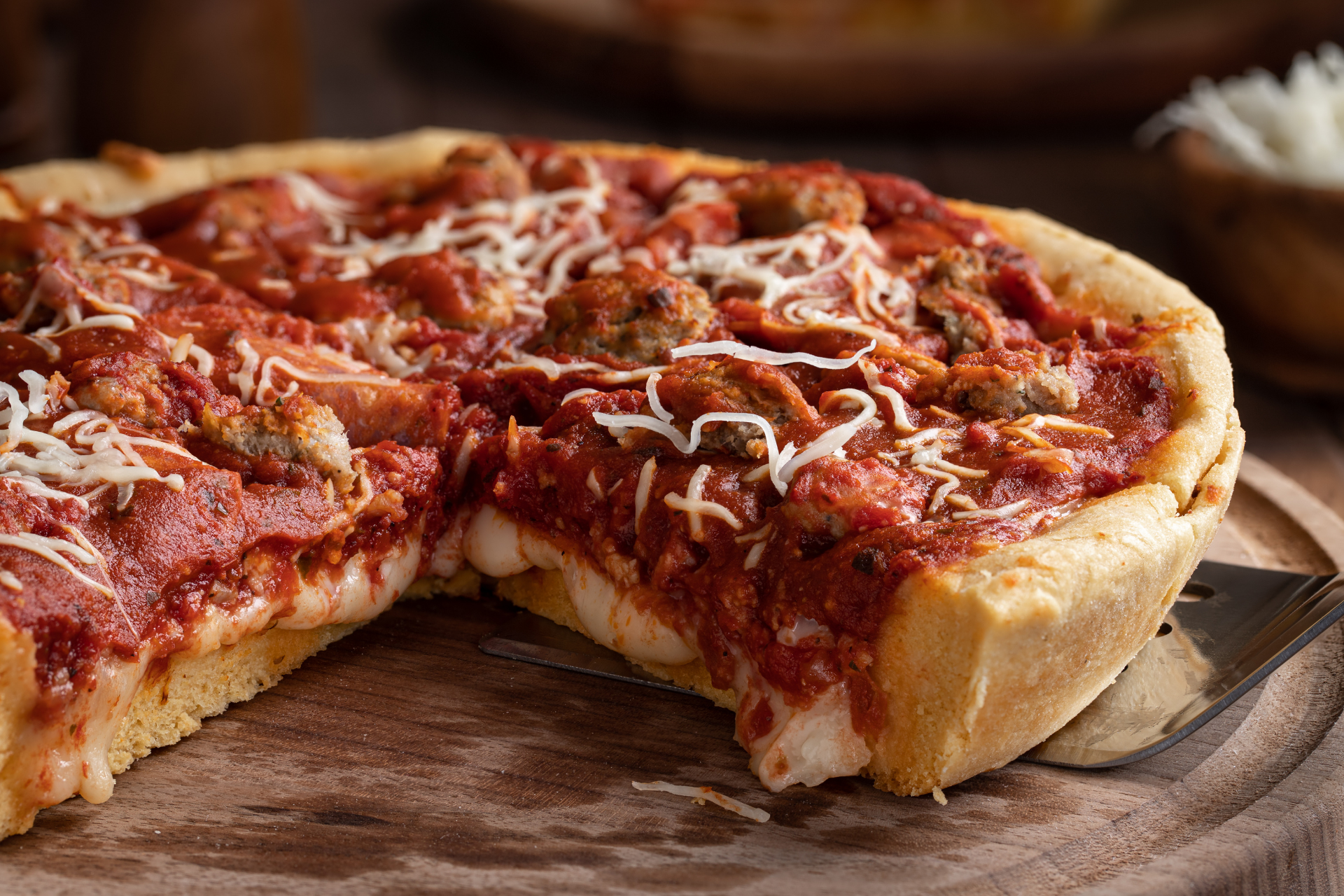 A pizza with a slice taken out of it is on a wooden cutting board.