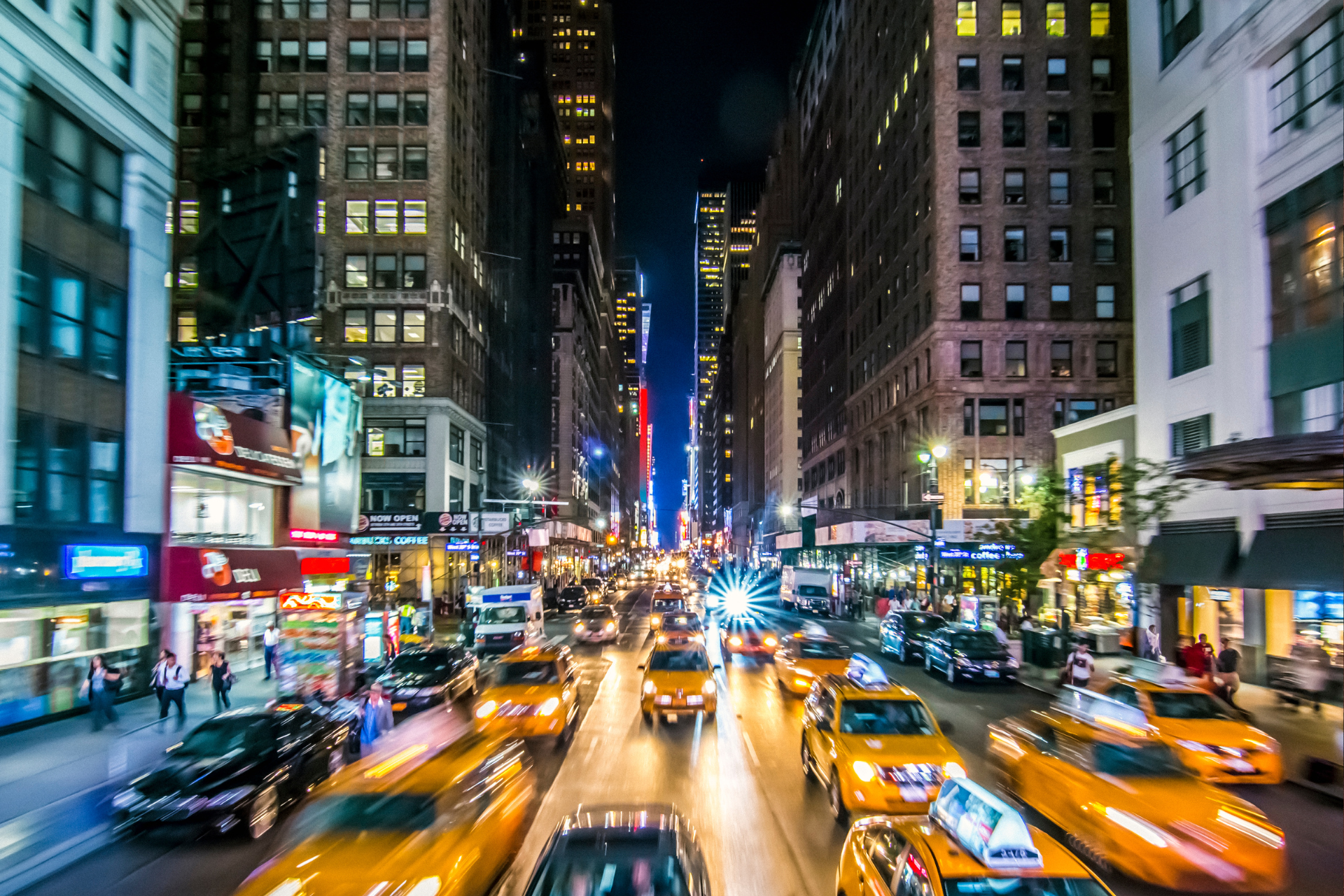 A busy city street at night with taxis driving down it.