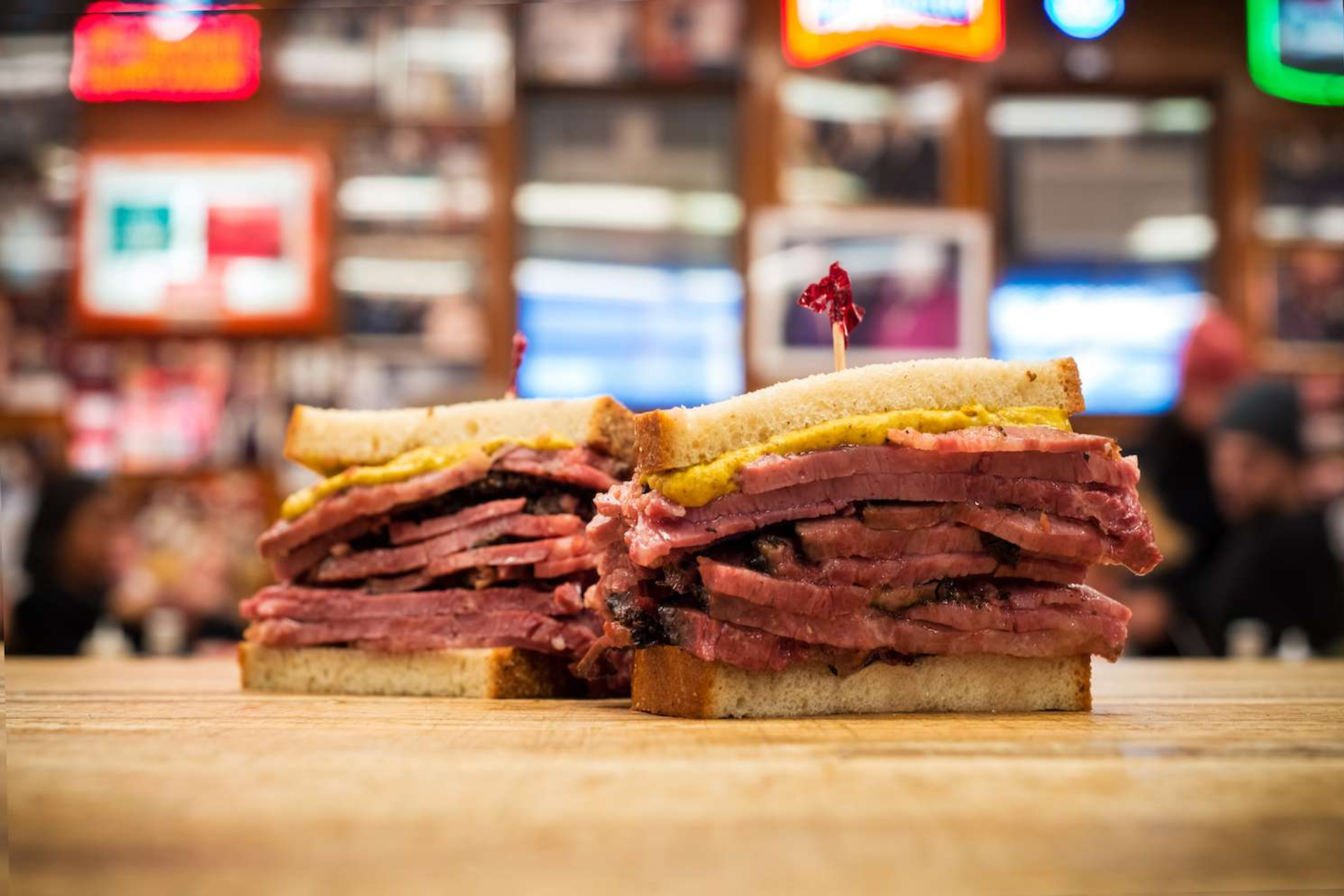 Two corned beef sandwiches are sitting on a wooden table.