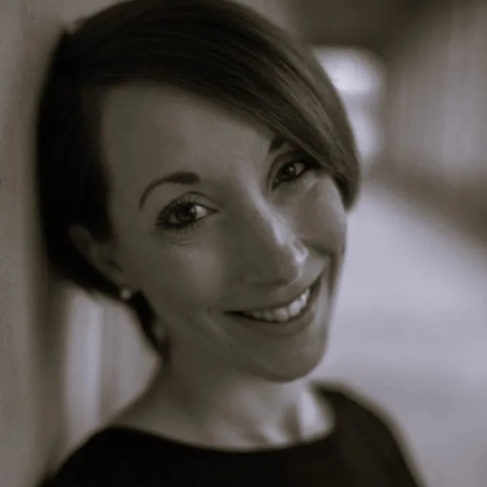 A woman is smiling in a black and white photo while leaning against a wall.