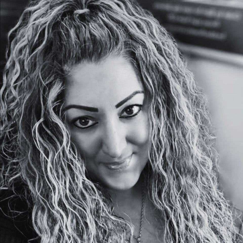 A woman with long curly hair is smiling in a black and white photo.