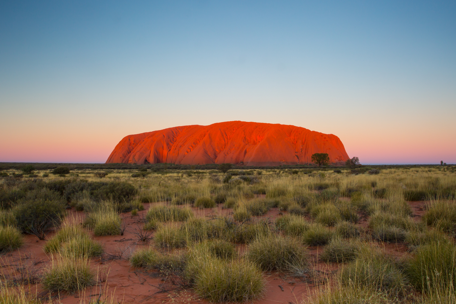 A large rock formation in the middle of a desert at sunset.