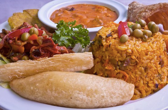 A plate of food with rice , vegetables , bread and sauce on a table.