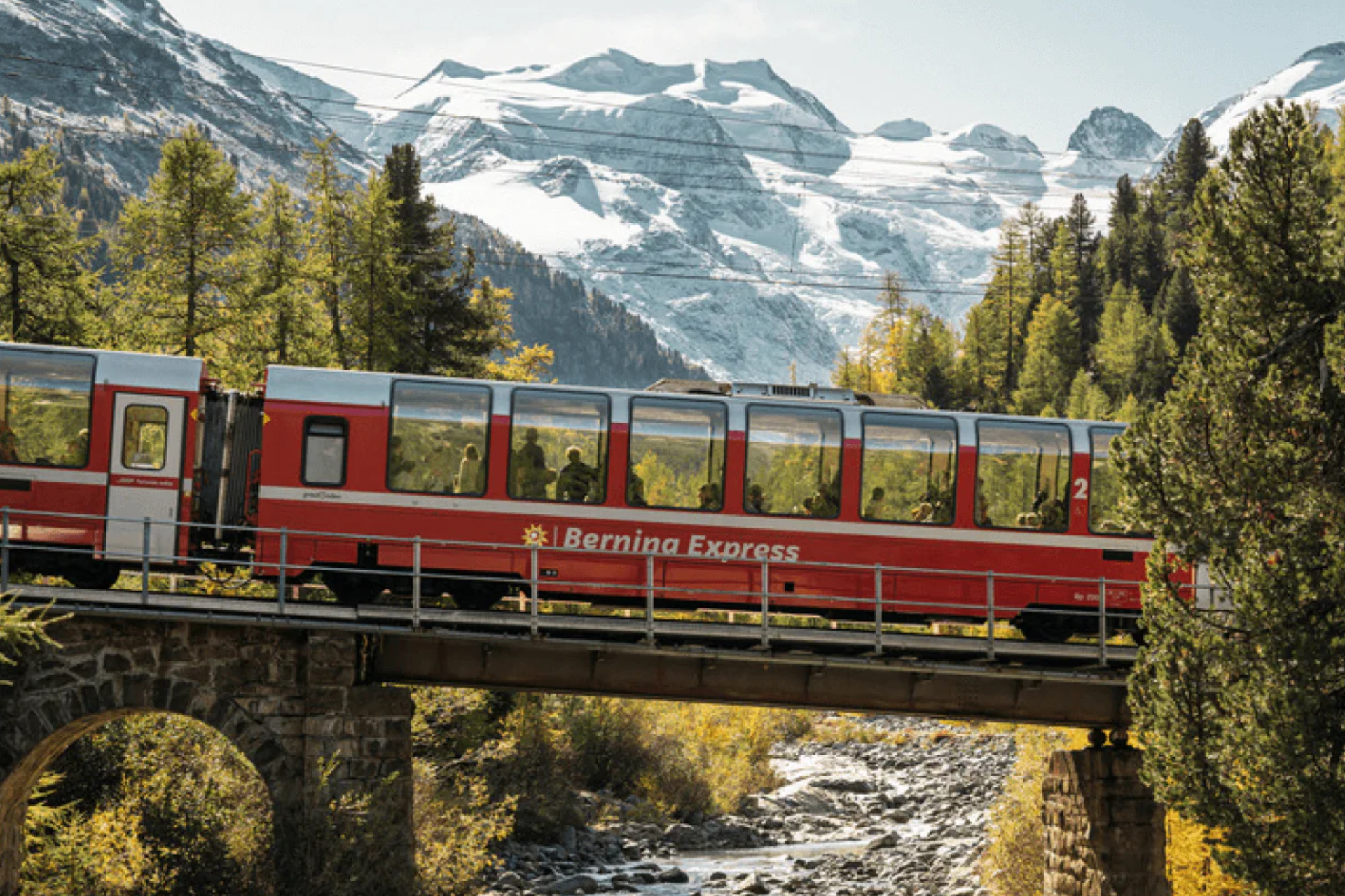 A red train is going over a bridge in the mountains.