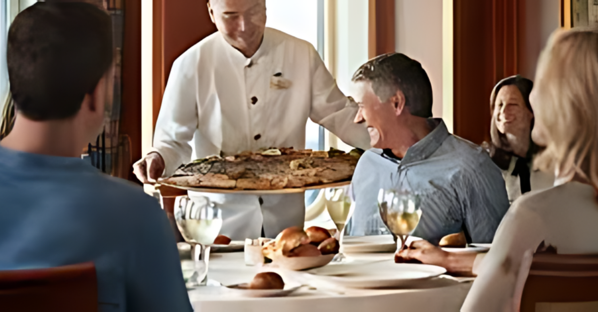 A group of people are sitting at a table in a restaurant while a chef serves them food.