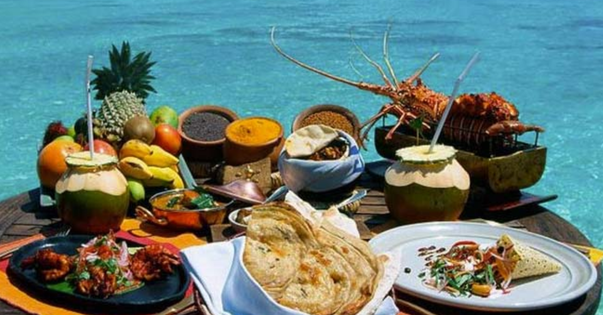 A table topped with plates of food and fruit in front of a body of water.