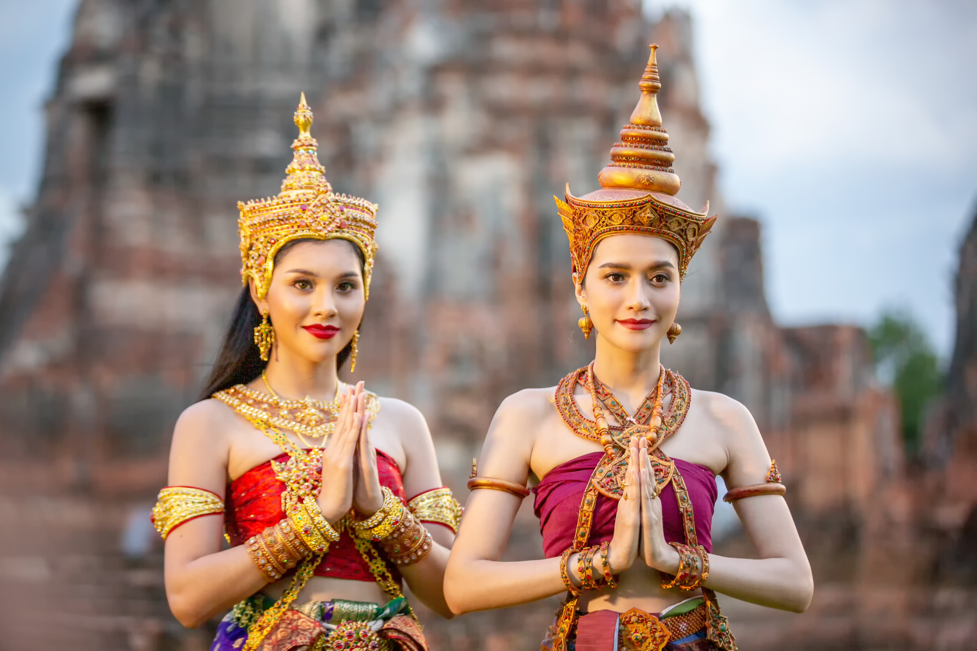 Two women in traditional thai costumes are standing next to each other in front of a temple.