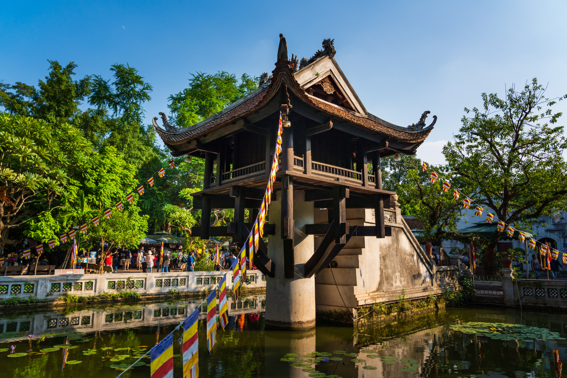 A pagoda is sitting on top of a bridge over a pond surrounded by trees.