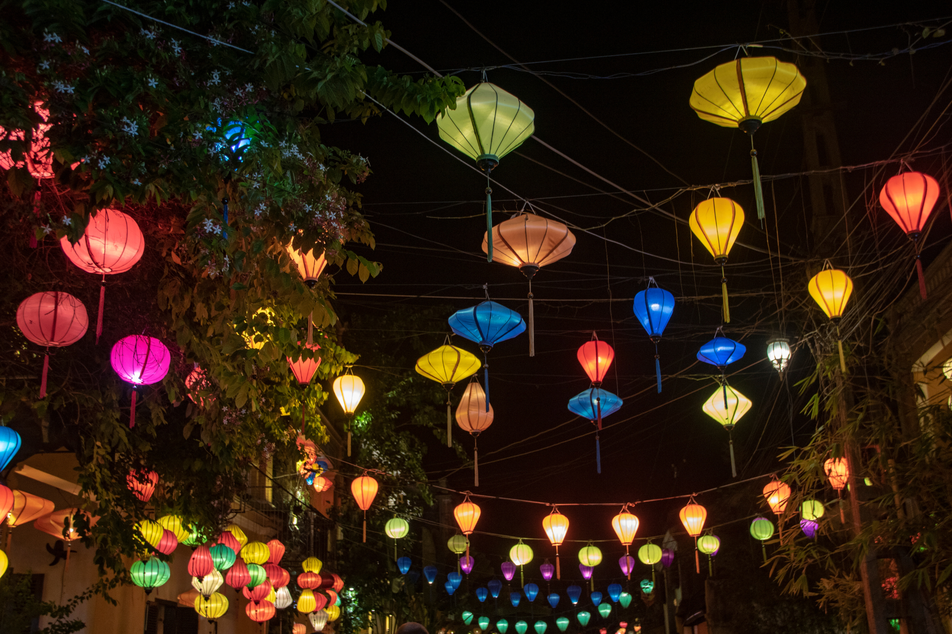 A bunch of colorful lanterns are hanging from a wire at night.