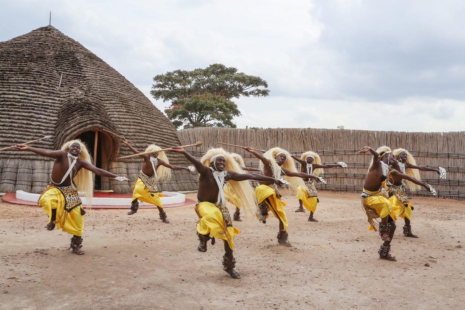 A group of men are dancing in front of a hut.