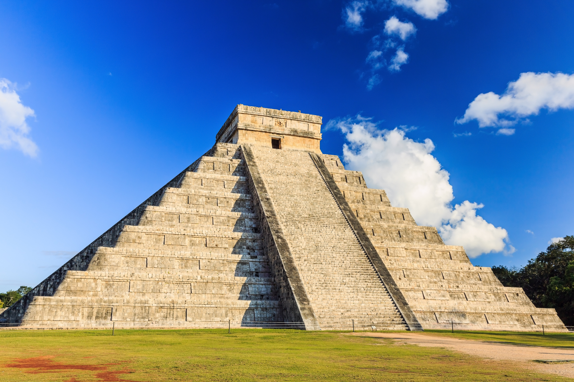 A large stone pyramid is sitting in the middle of a grassy field.