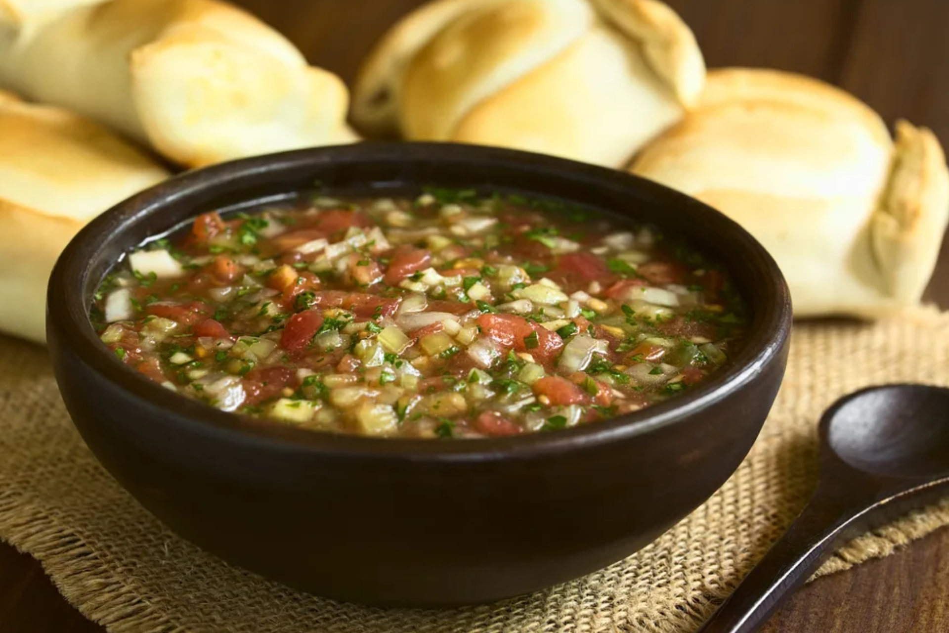 A bowl of soup with a wooden spoon next to some pastries.