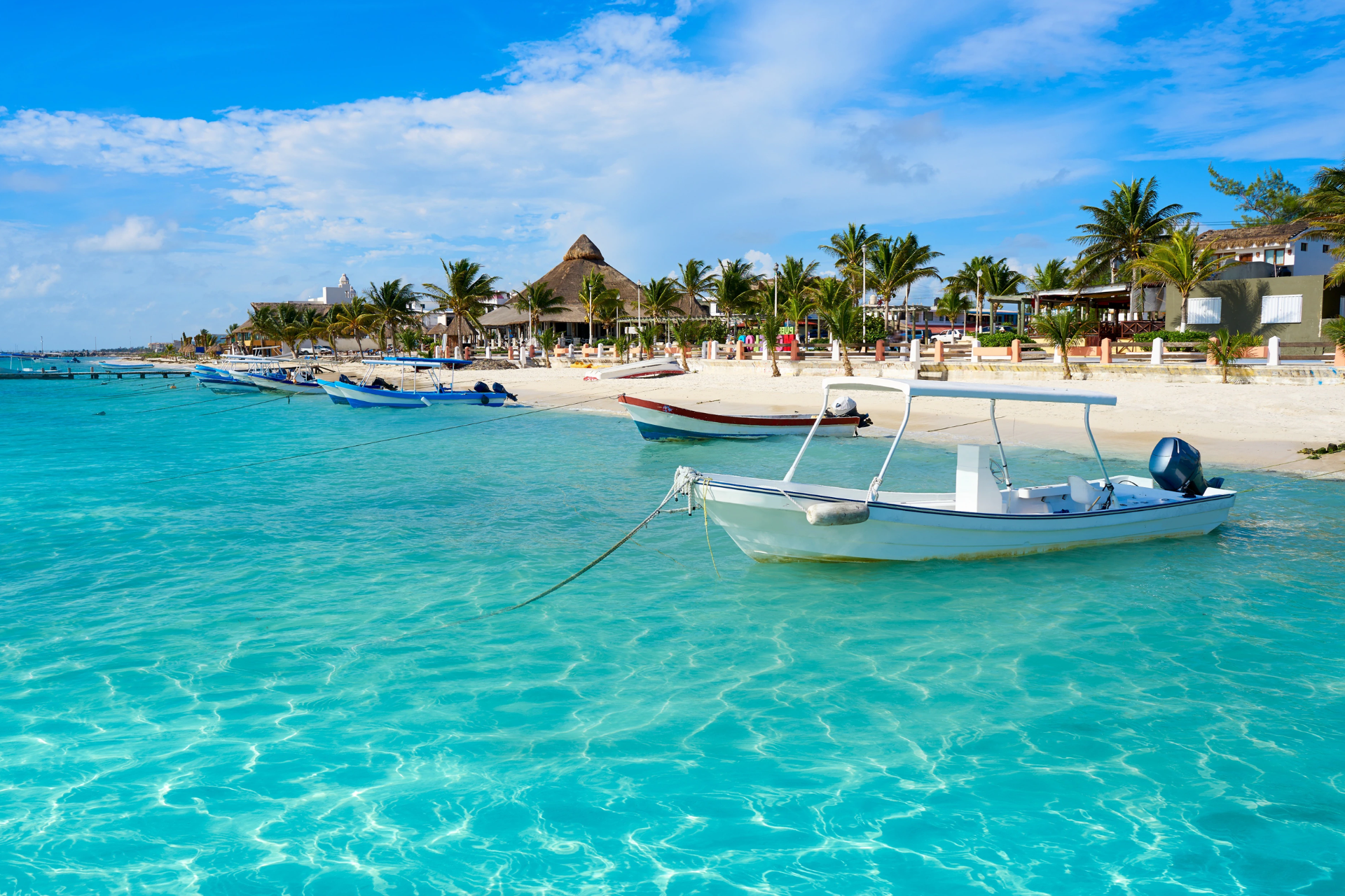 A white boat is docked in the ocean near a beach.