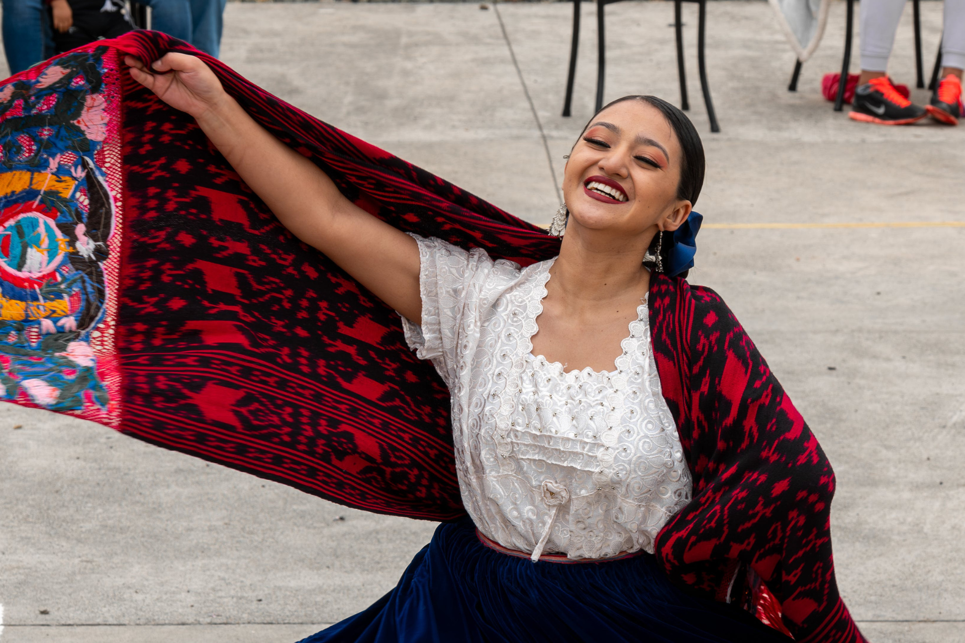 A woman in a white shirt and blue skirt is holding a red and black scarf.