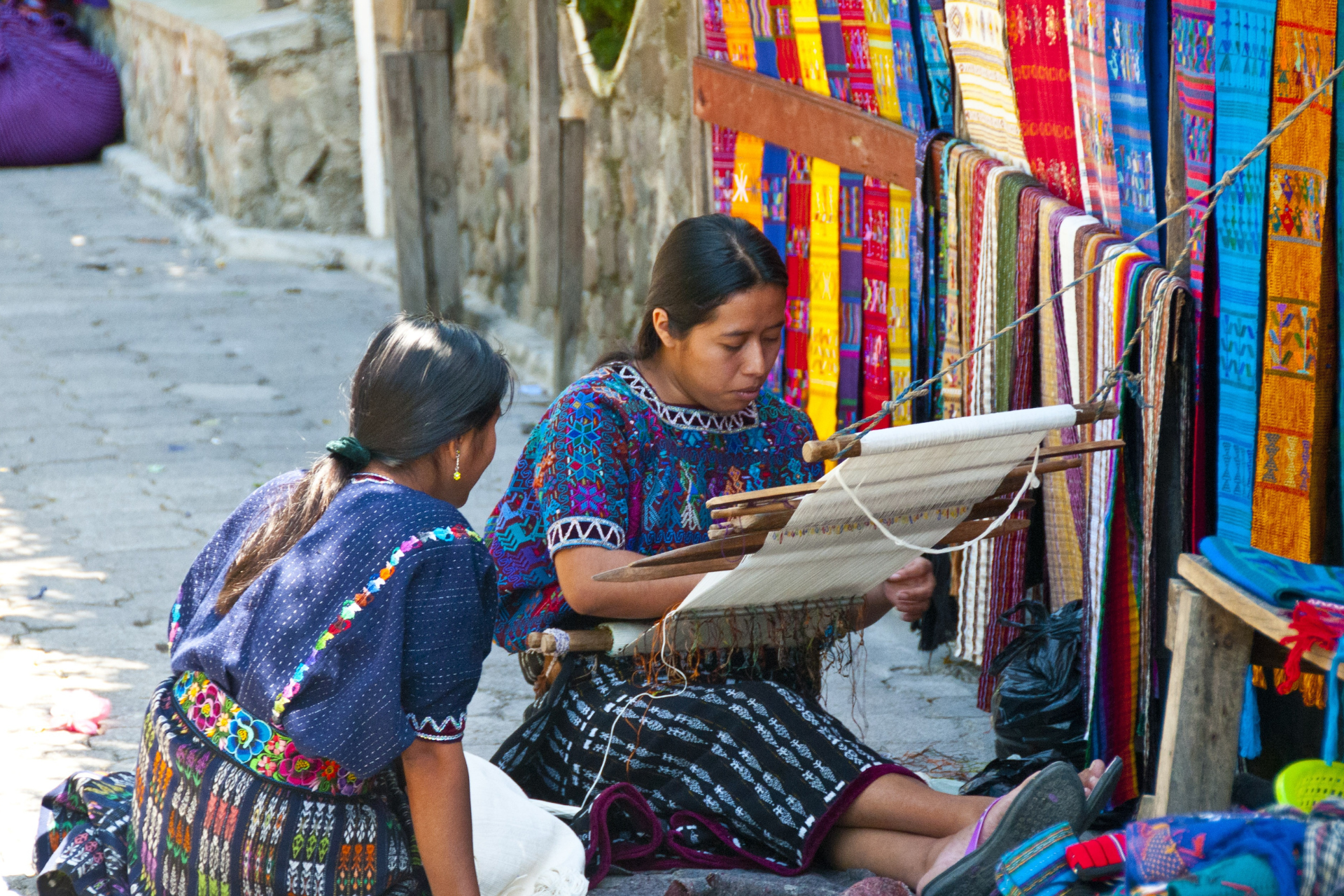 Two women are sitting next to each other in front of a loom.