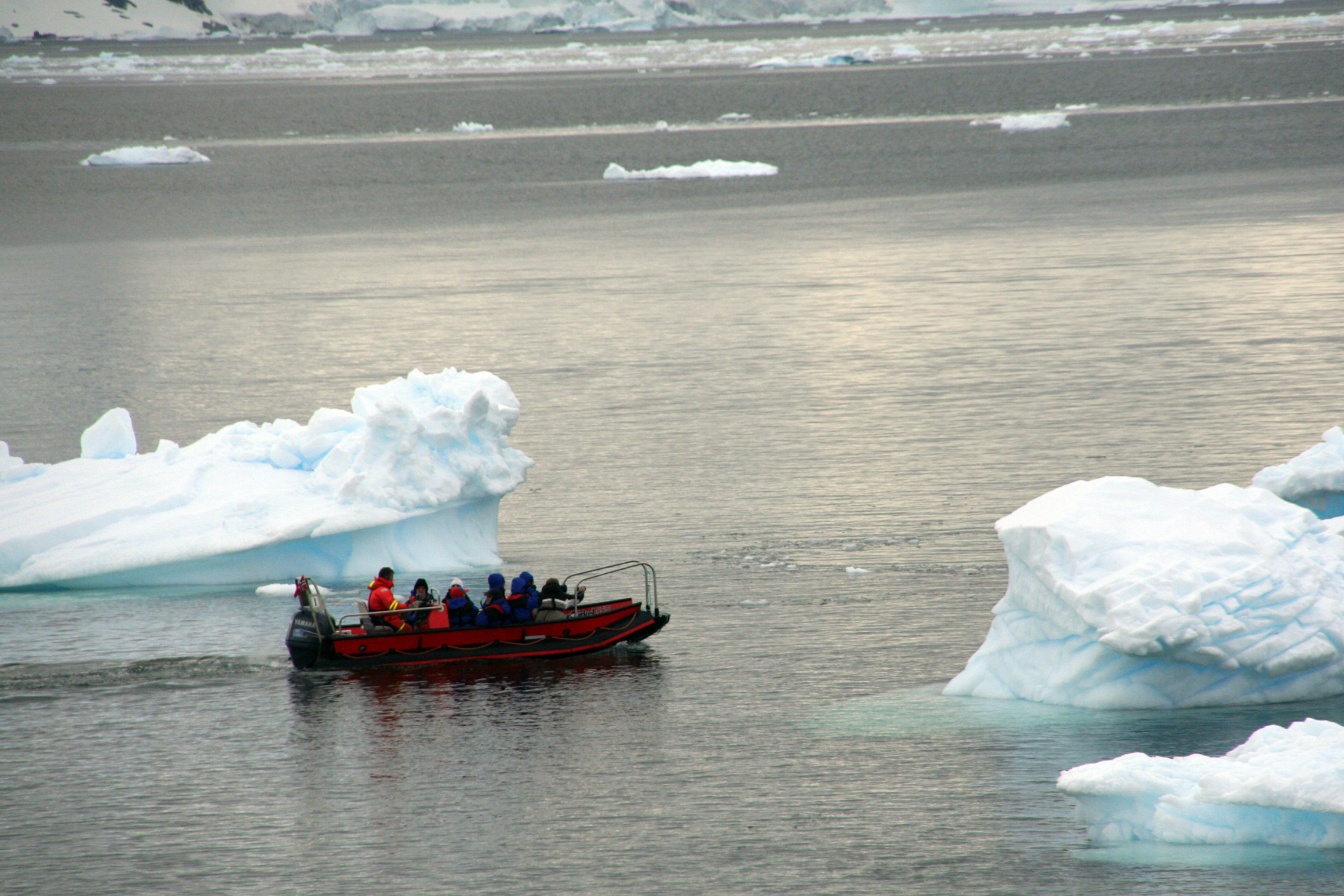 A boat with people in it is in the water near icebergs