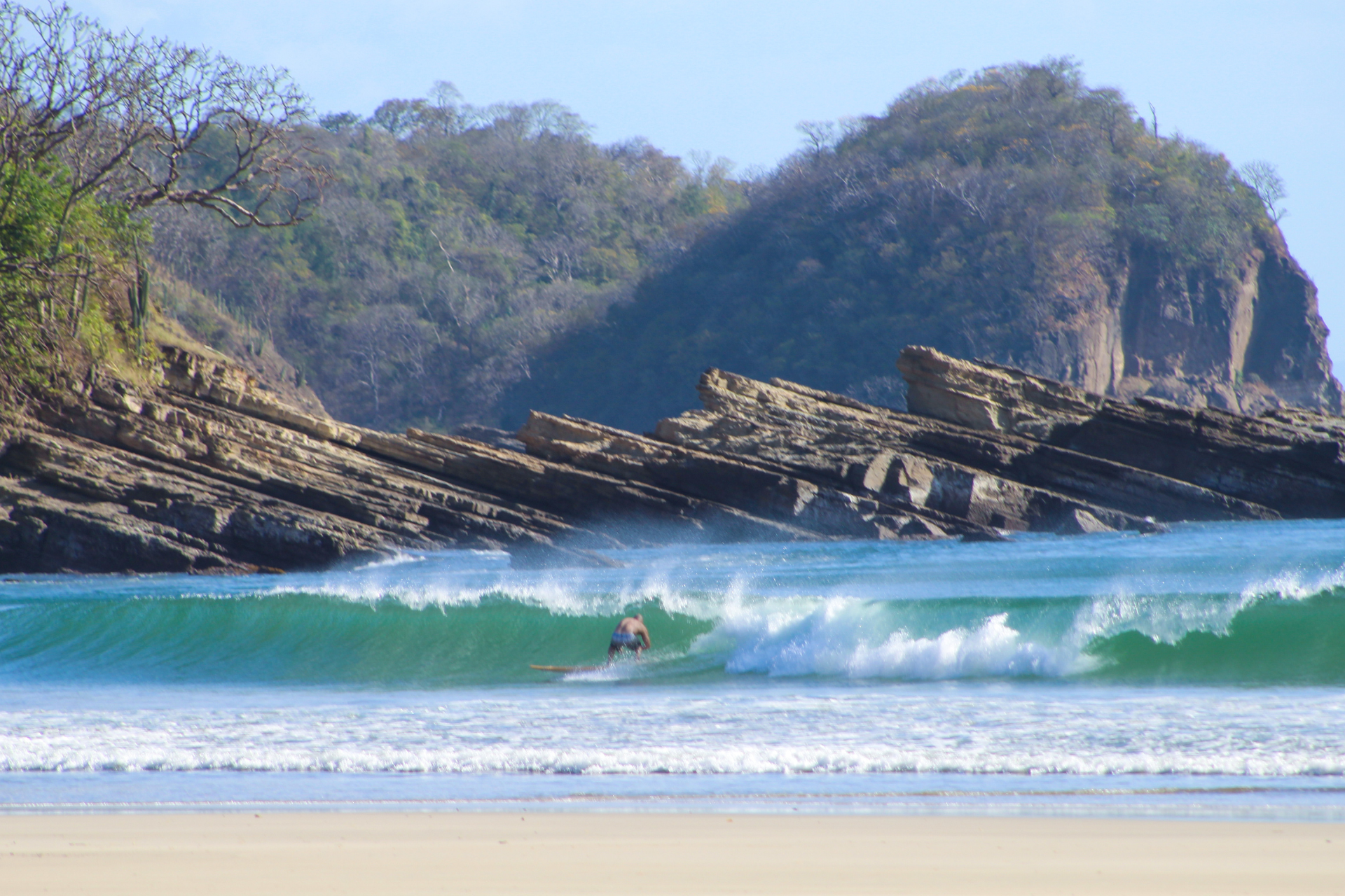 A person is riding a wave on a surfboard on a beach.