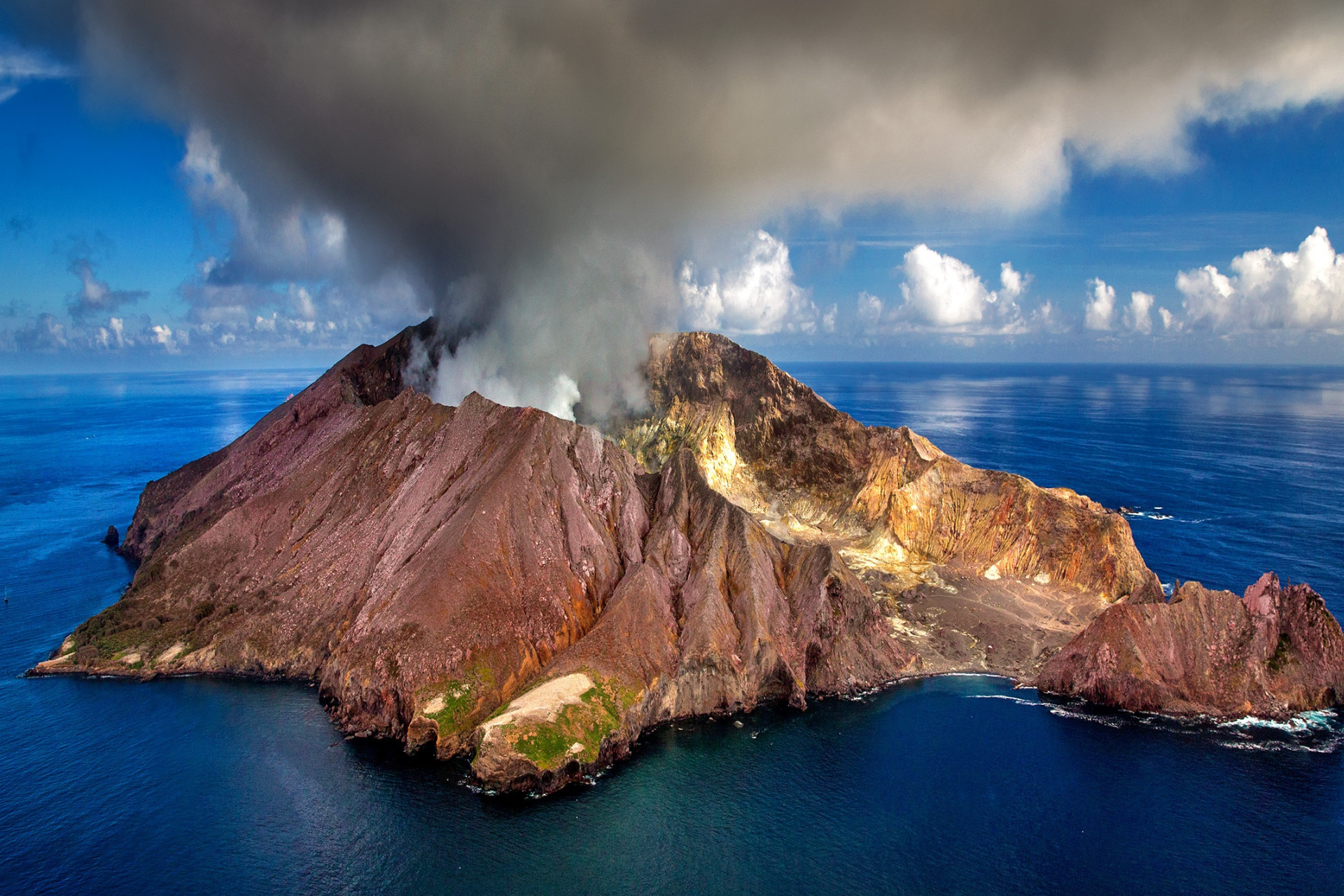 An aerial view of a volcano erupting in the ocean.