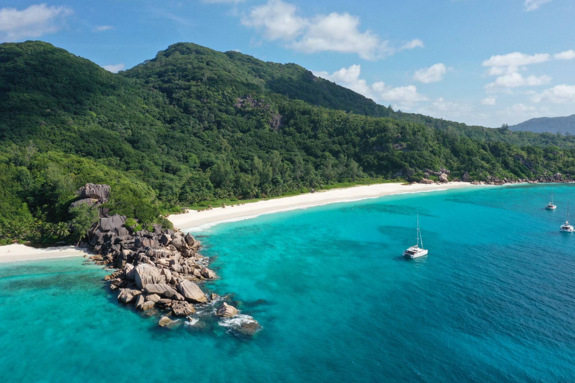 An aerial view of a beach with boats in the water and mountains in the background.