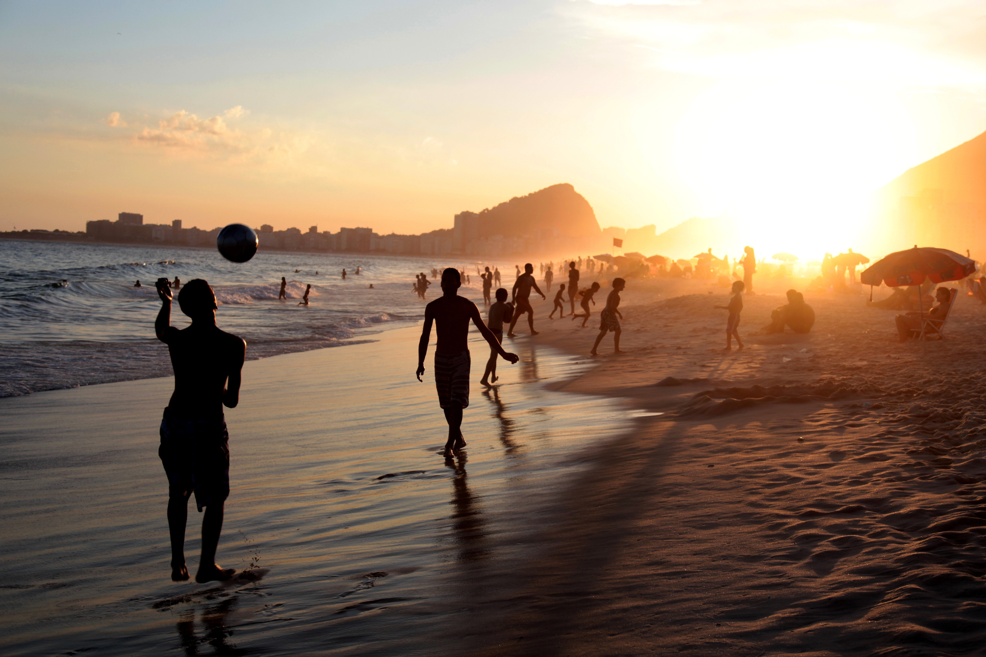 A group of people are playing soccer on the beach at sunset.