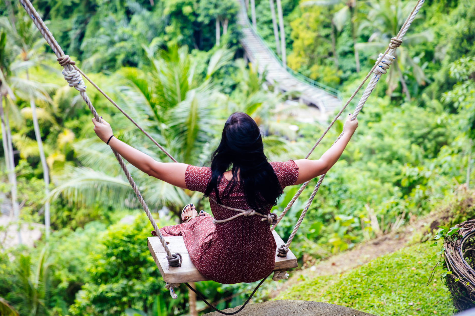 A woman is sitting on a swing in the jungle.