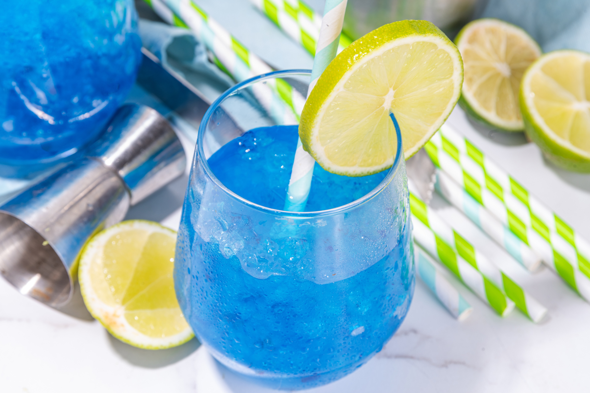 A blue drink with a straw and lime slices in a glass.