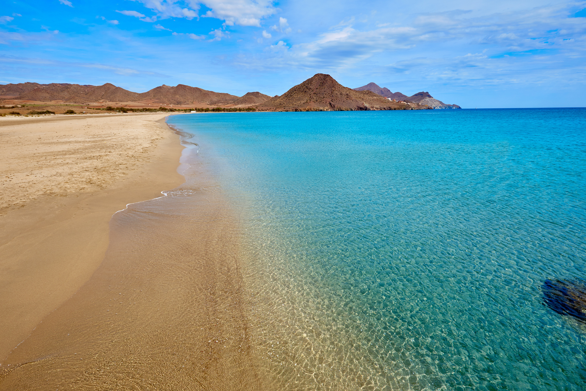 A beach with mountains in the background and a clear blue ocean.