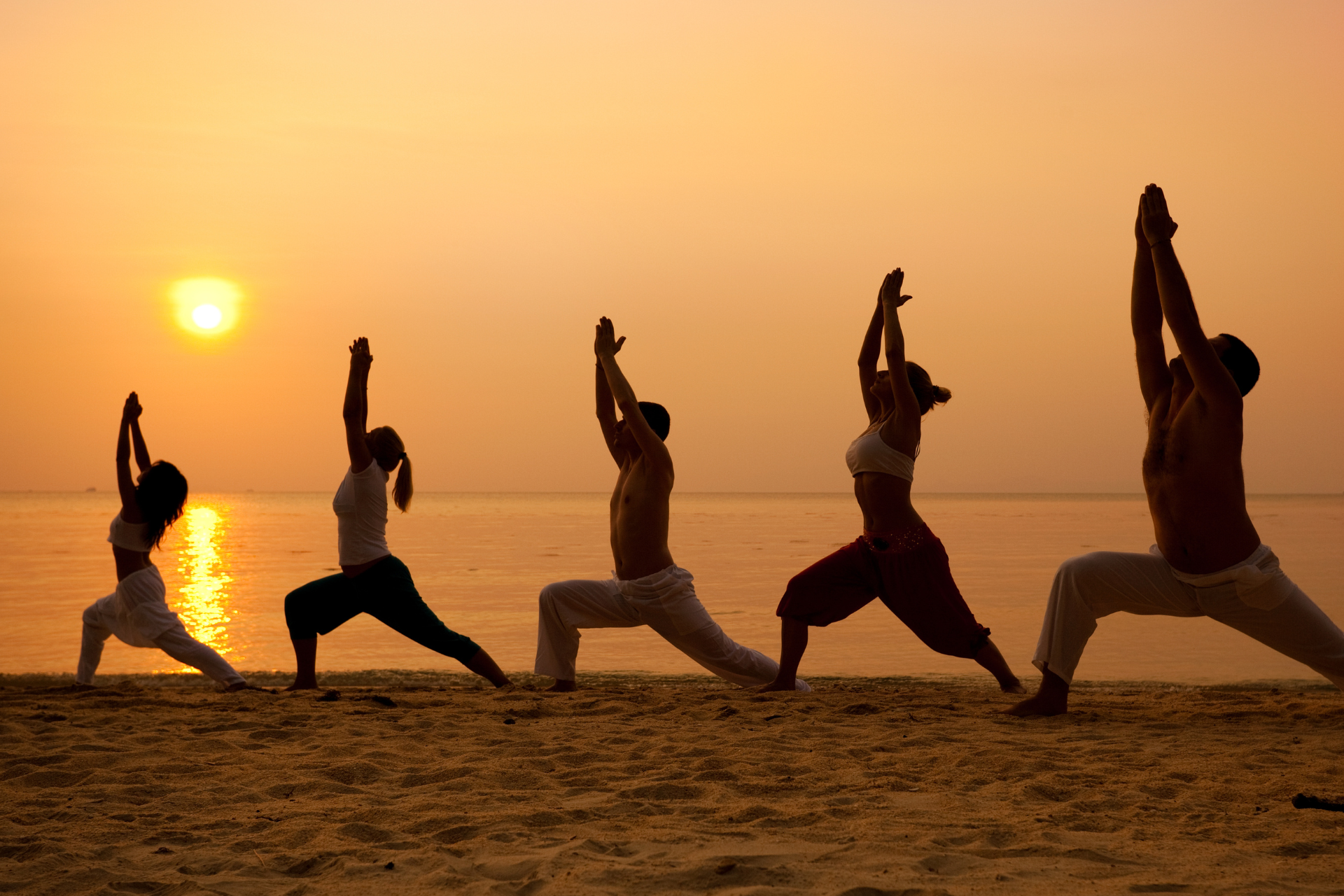 A group of people are practicing yoga on the beach at sunset