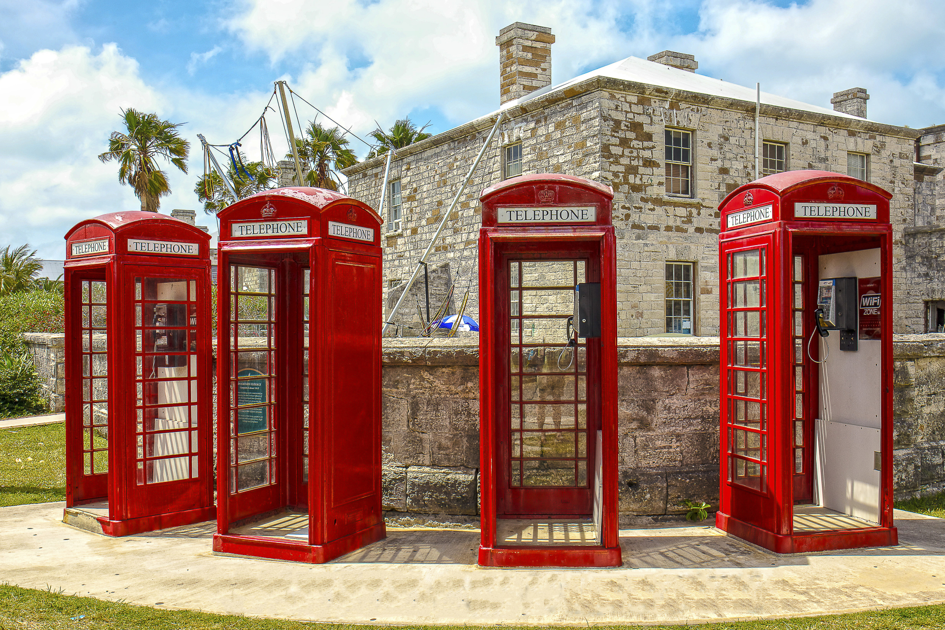 A row of red telephone booths are lined up in front of a stone building.