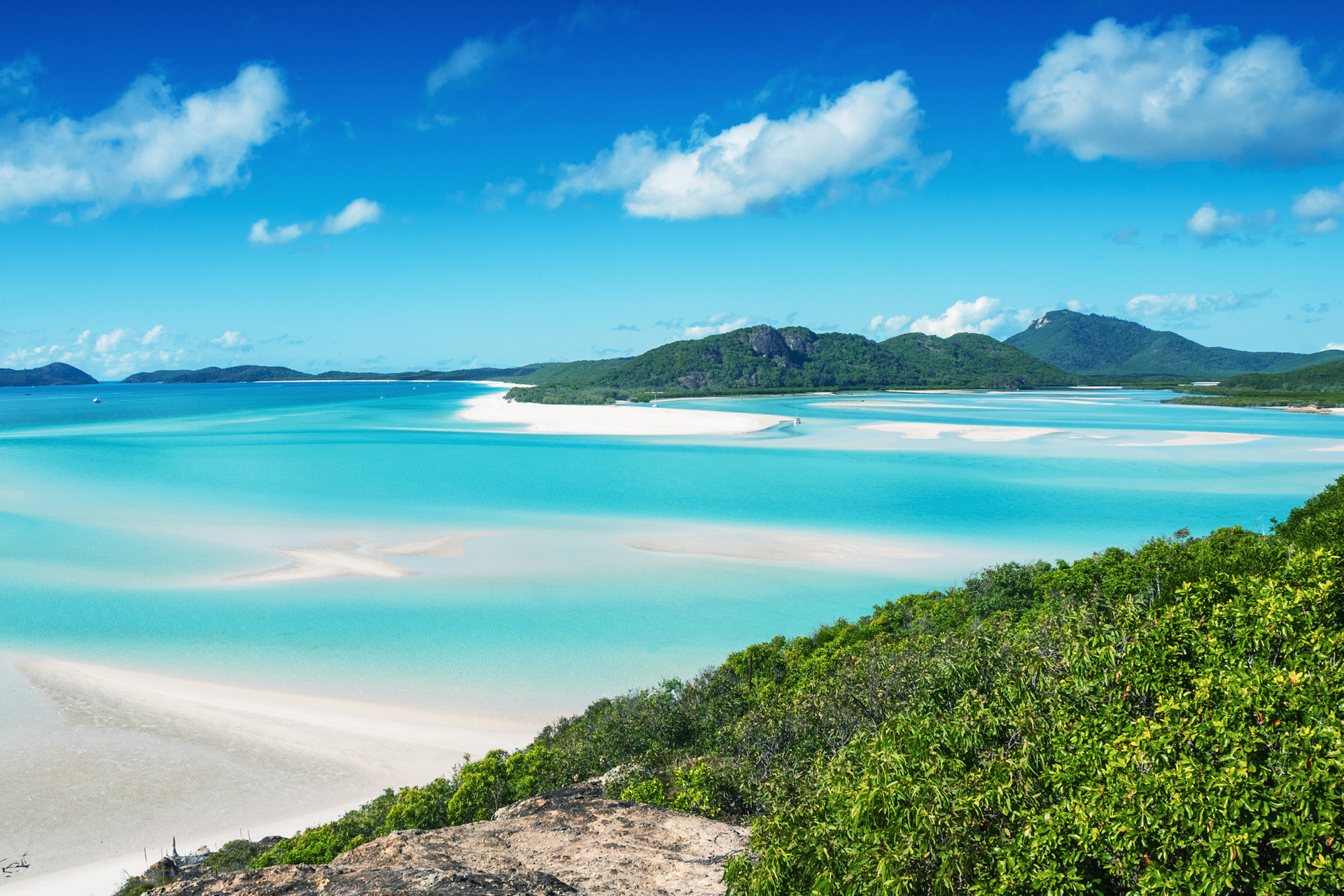 A view of a tropical beach with a blue ocean and mountains in the background.