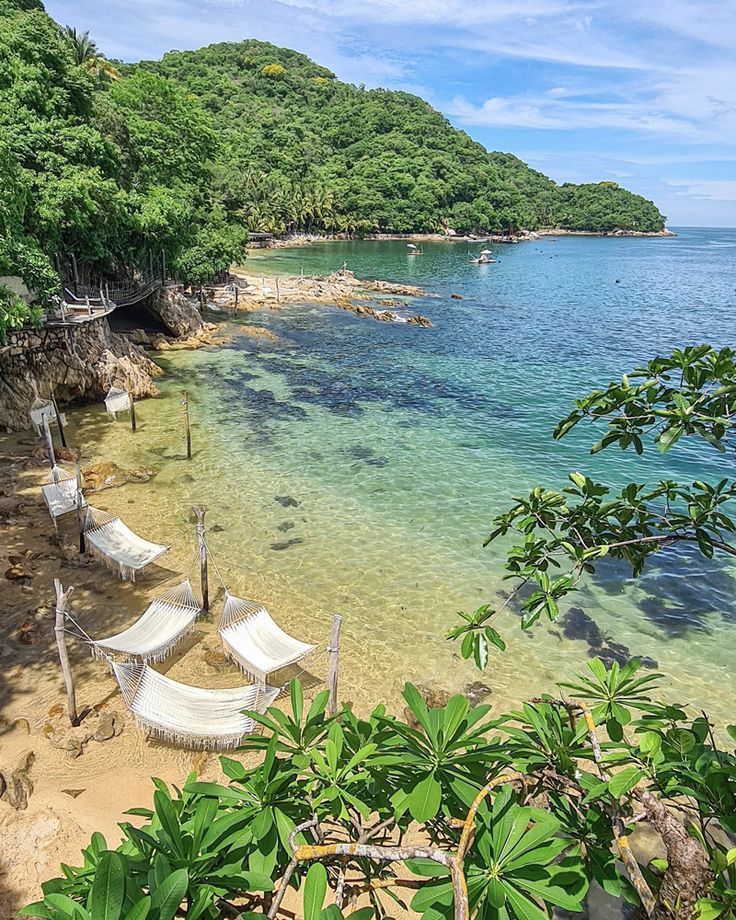 There are many hammocks on the beach near the water.