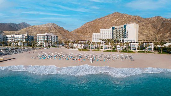 An aerial view of a beach with a hotel in the background and mountains in the background.