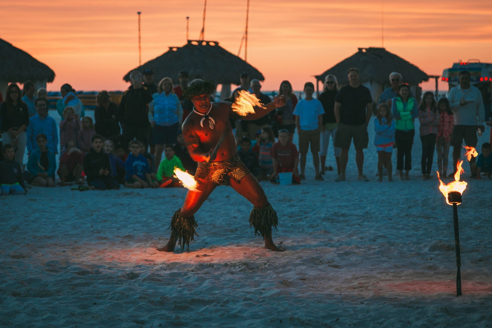 A man is playing with fire on the beach while a crowd watches.