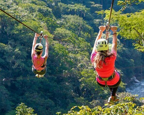 Two women are flying through the air on a zip line.