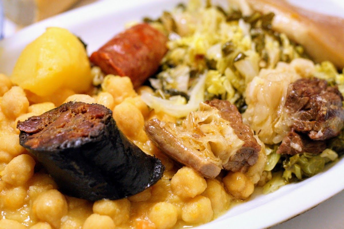 A white plate topped with chickpeas , meat and vegetables.