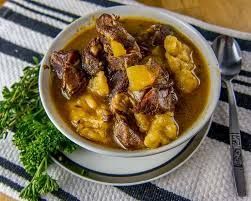 A bowl of soup with meat and beans on a plate with a spoon.