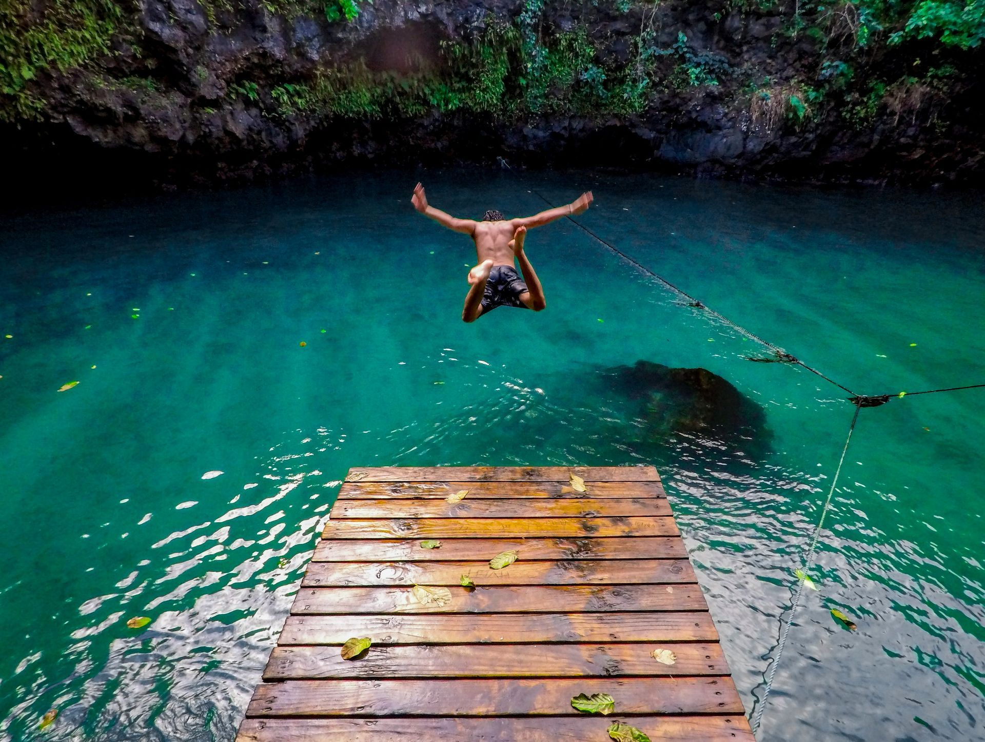 A man is jumping into a body of water from a wooden dock.