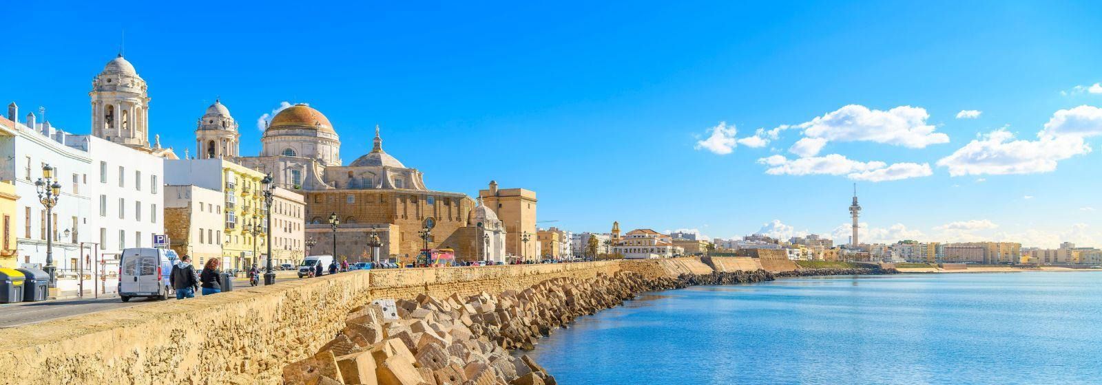 A city along the shore of a body of water with buildings and a blue sky in the background.