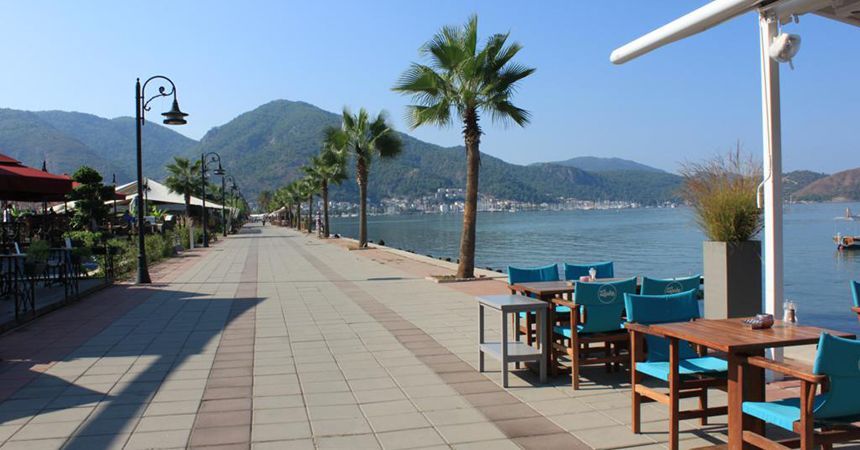 A row of tables and chairs on a sidewalk next to a body of water.