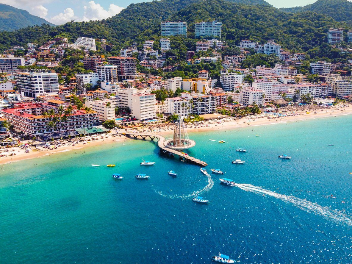 An aerial view of a beach with boats in the water and a city in the background.