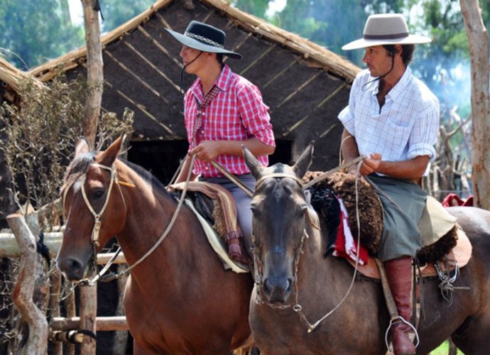 Two men are riding horses in front of a hut