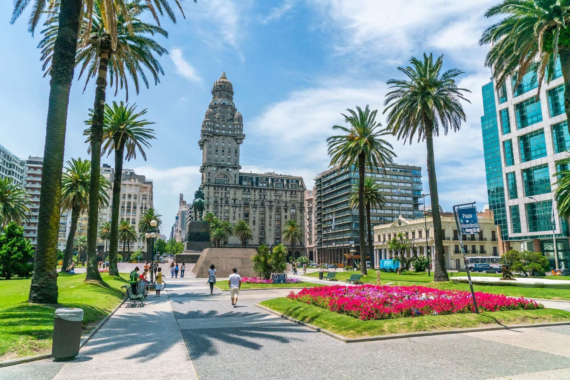 A city park with palm trees and flowers in front of a building.