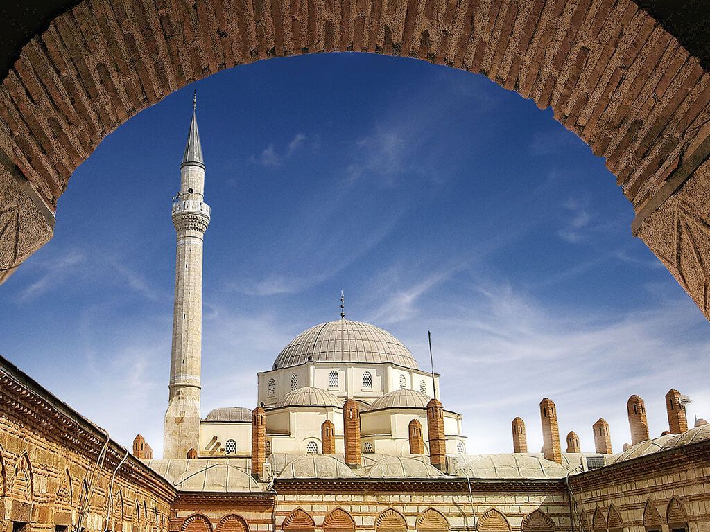 A mosque with a very tall minaret is seen through an archway