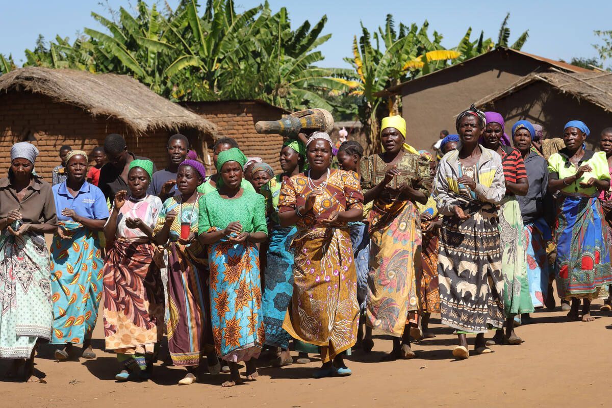 A group of women are standing in front of a thatched hut.