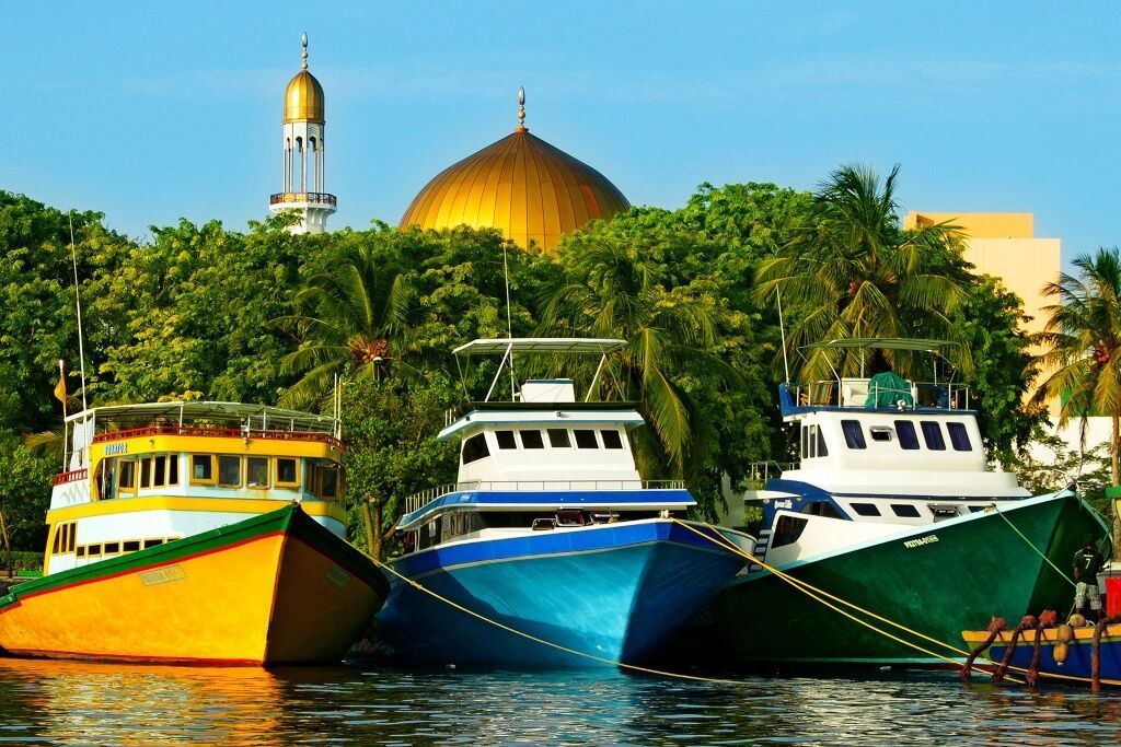 Three boats are tied to a dock with a mosque in the background